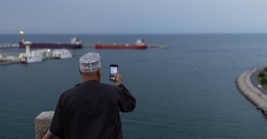 A man takes a photo with his mobile phone as vessels sit at anchor amid the U.S.-Israeli conflict with Iran, in Sultan Qaboos Port in Muscat, Oman, March 26, 2026. (Reuters Photo)