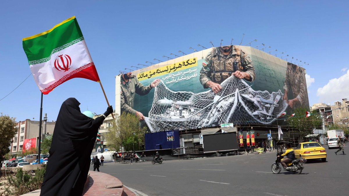 A woman holds Iran’s national flag while standing near a billboard with a sentence reading ‘The Strait of Hormuz remains closed’ at the Iqelab Square in Tehran, Iran, April 5, 2026. (AFP Photo)
