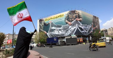 A woman holds Iran’s national flag while standing near a billboard with a sentence reading ‘The Strait of Hormuz remains closed’ at the Iqelab Square in Tehran, Iran, April 5, 2026. (AFP Photo)
