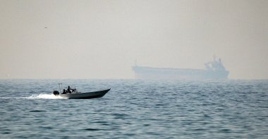 A motorboat cruises along the shore off the town of al-Jeer on the Strait of Hormuz in the northern emirate of Ras al-Khaimah, with a tanker seen in the background, UAE, Feb. 25, 2026. (AFP Photo)