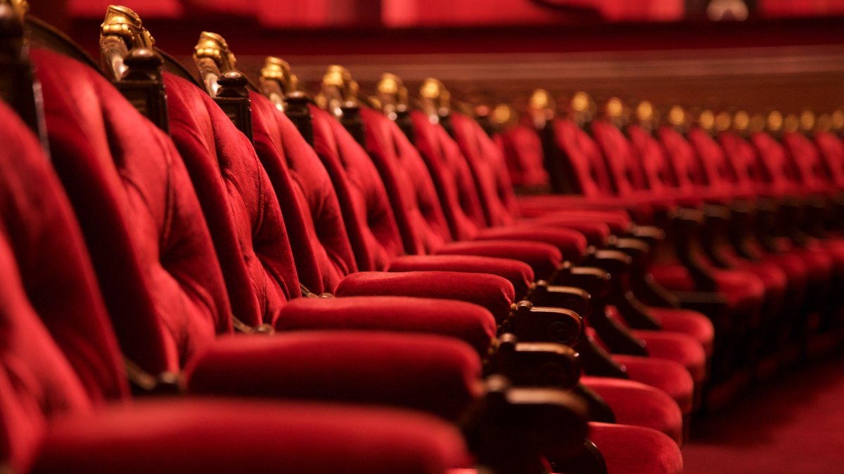 Rows of plush red velvet opera chairs with ornate gold trim. (Shutterstock Photo)