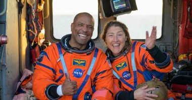 NASA astronauts Victor Glover (L) and Christina Koch sit on a Navy MH-60 Seahawk helicopter on the flight deck of USS John P. Murtha after they and fellow crewmates were extracted from their Orion spacecraft after splashdown, in the Pacific Ocean off the coast of California, U.S., April 10, 2026. (AFP Photo)