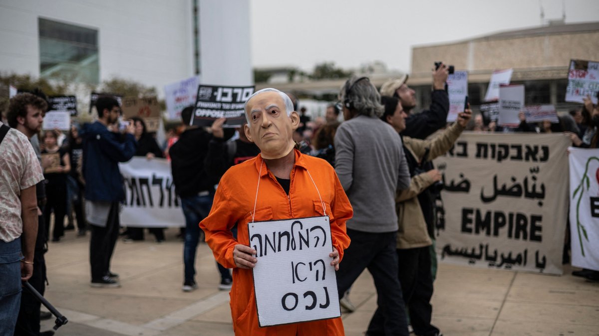 A protestor wearing a face mask of Israeli Prime Minister Benjamin Netanyahu holds a banner that reads "war is an asset" during an anti-war protest, Tel Aviv, Israel, March 14, 2026. (AFP Photo)