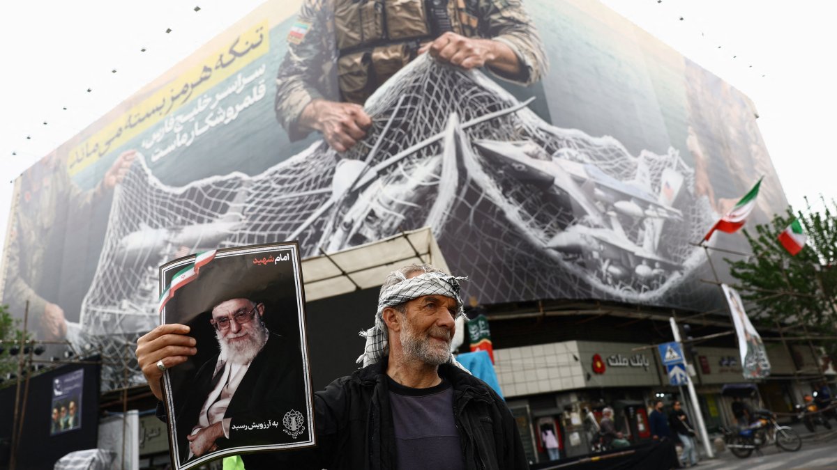A man holds a picture of the late Supreme Leader of Iran Ayatollah Ali Khamenei, next to an anti-U.S. billboard, on a street in Tehran, Iran, April 12, 2026. (Reuters Photo)