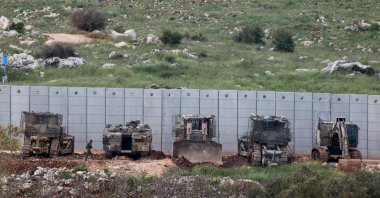 An Israeli soldier walks near armored military engineering vehicles on the Israeli side of the border, April 12, 2026. (Reuters Photo)