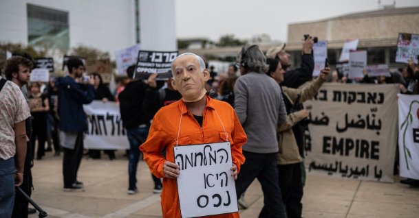A protestor wearing a face mask of Israeli Prime Minister Benjamin Netanyahu holds a banner that reads "war is an asset" during an anti-war protest, Tel Aviv, Israel, March 14, 2026. (AFP Photo)