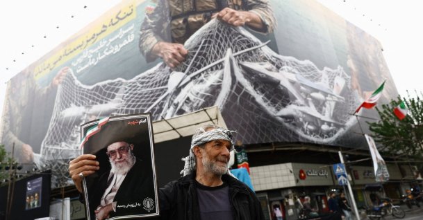 A man holds a picture of the late Supreme Leader of Iran Ayatollah Ali Khamenei, next to an anti-U.S. billboard, on a street in Tehran, Iran, April 12, 2026. (Reuters Photo)