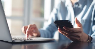 A businesswoman using a mobile smartphone and working on a laptop computer at an office. (Shutterstock Photo)