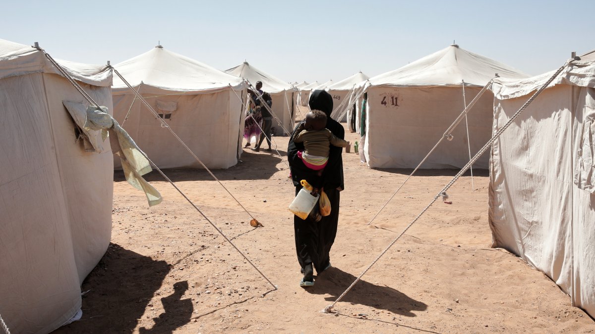 A Sudanese woman displaced from el-Fasher carries her child as she walks between tents at the newly established el-Afadh camp in al Dabbah, northern Sudan, Nov. 16, 2025. (AP Photo)
