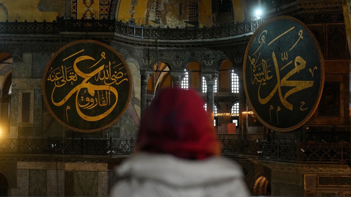 A visitor looks toward large Islamic calligraphy medallions bearing the names of Prophet Muhammad, right, and Caliph Omar, left, inside the Hagia Sophia mosque in Istanbul, Türkiye, Feb, 27, 2026. (AP Photo)