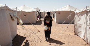 A Sudanese woman displaced from el-Fasher carries her child as she walks between tents at the newly established el-Afadh camp in al Dabbah, northern Sudan, Nov. 16, 2025. (AP Photo)
