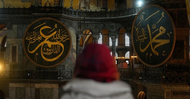 A visitor looks toward large Islamic calligraphy medallions bearing the names of Prophet Muhammad, right, and Caliph Omar, left, inside the Hagia Sophia mosque in Istanbul, Türkiye, Feb, 27, 2026. (AP Photo)
