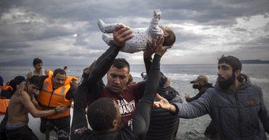 A volunteer holds up a baby as others help migrants and refugees disembark from a dinghy after their arrival on the island of Lesbos, Greece, Nov. 25, 2015. (AP Photo)