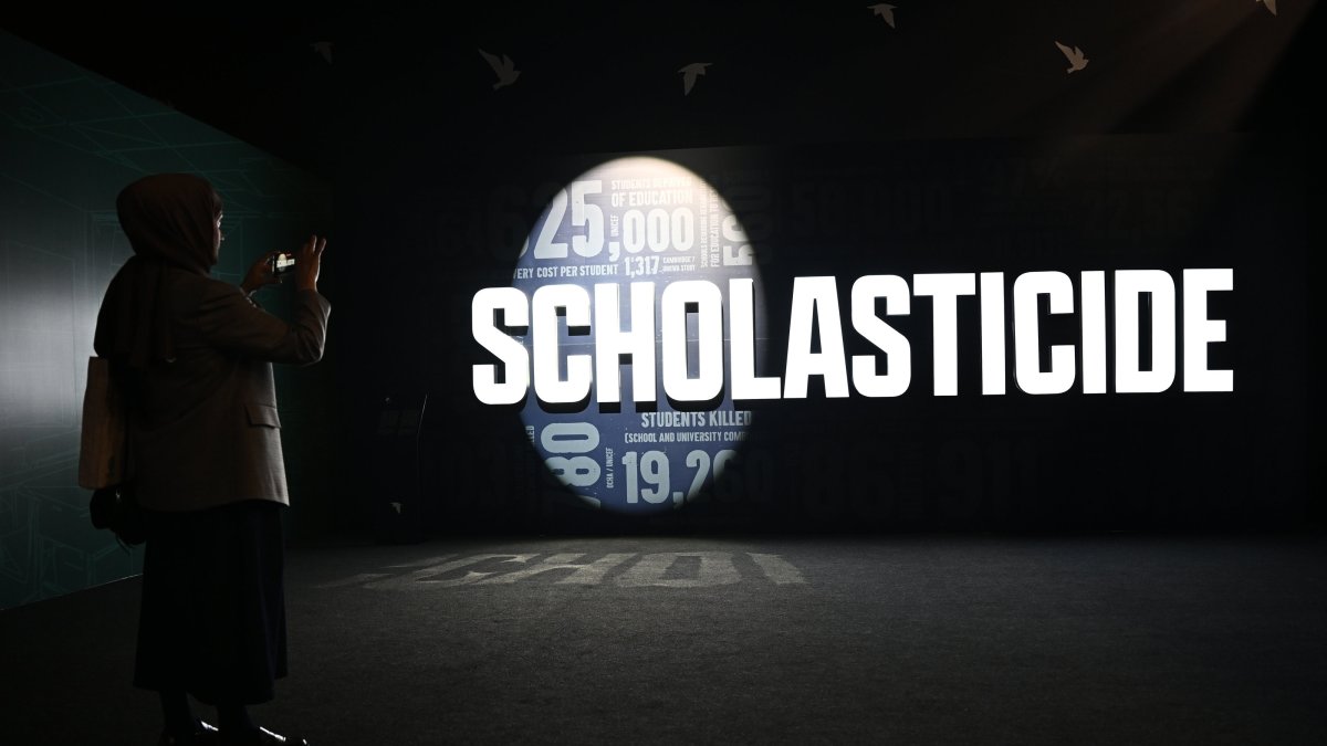 A visitor photographs the word “scholasticide” projected on a wall at an exhibition at the Antalya Diplomacy Forum, Antalya, southern Türkiye, April 17, 2026. (Photo by Dilek Yalçın)