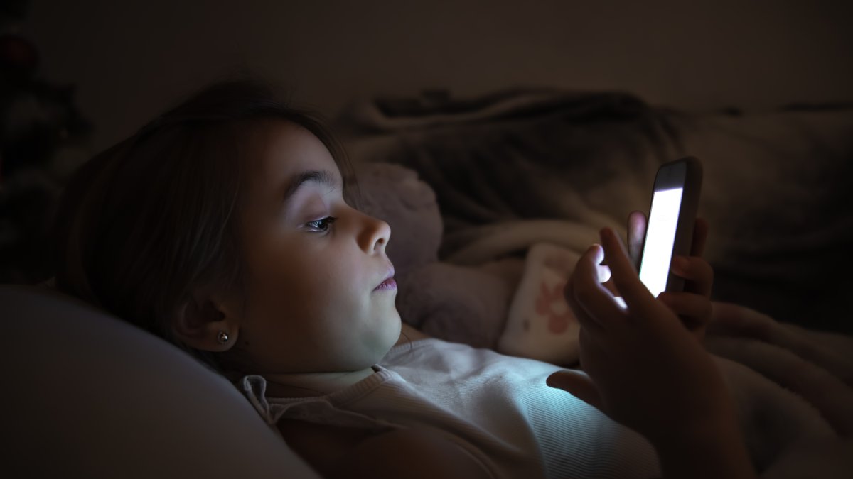 A  little girl lies in bed and plays on the phone at night. (Shutterstock Photo) 