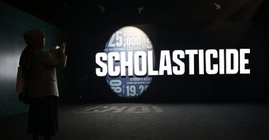 A visitor photographs the word “scholasticide” projected on a wall at an exhibition at the Antalya Diplomacy Forum, Antalya, southern Türkiye, April 17, 2026. (Photo by Dilek Yalçın)