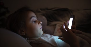 A  little girl lies in bed and plays on the phone at night. (Shutterstock Photo) 