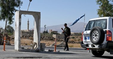 A United Nations Disengagement Observatory Force (UNDOF) vehicle drives past a member of Syria's security forces standing guard outside a former army base near the city of Quneitra in southern Syria, on the edge of the Israeli-occupied Golan Heights, Sept. 21, 2025. (AFP File Photo)