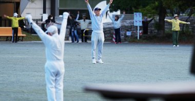 People perform a stretching exercise while listening to music and guidance from radio at a public park, Tokyo, Japan, April 6, 2026. (AP Photo)
