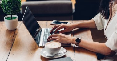 A working woman using her laptop in a cafe with a coffee. (Shutterstock Photo)