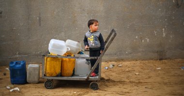 A displaced Palestinian boy stands on a trolley loaded with empty water canisters at the Nuseirat refugee camp, central Gaza Strip, Palestine, April 1, 2026. (AFP Photo)