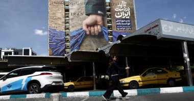 A woman walks past a billboard with a graphic design about the Strait of Hormuz on a building, in Tehran, Iran, April 27, 2026. (Reuters Photo)