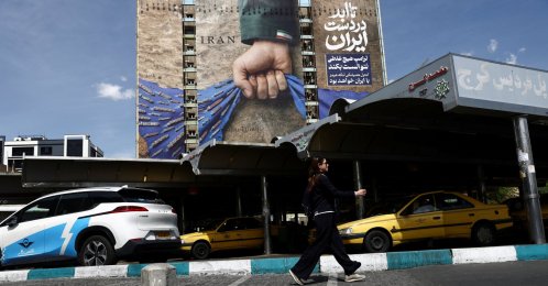 A woman walks past a billboard with a graphic design about the Strait of Hormuz on a building, in Tehran, Iran, April 27, 2026. (Reuters Photo)