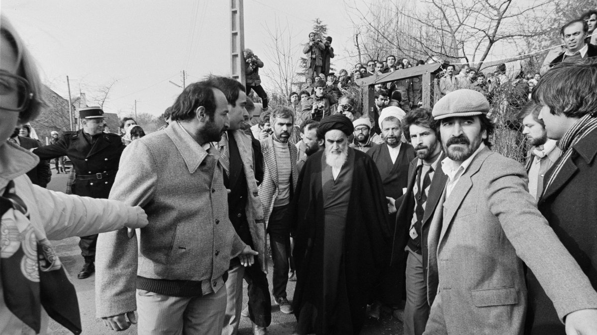 Followers form a human chain around the Ayatollah Ruhollah Khomeini, to protect him from the crowd massed as he walks back to his residence a few hours before leaving for Charles de Gaulle Airport where he is scheduled to fly to Tehran after more than 14 years in exile, in suburban Neauphle-le-Chateau, outside Paris, France, Jan. 31, 1979. (AP Photo)