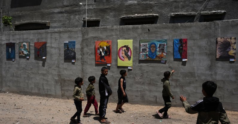 Children look at paintings by Palestinian artists during an exhibition in al-Bureij camp in the central Gaza Strip, Palestine, April 28, 2026. (AP Photo)