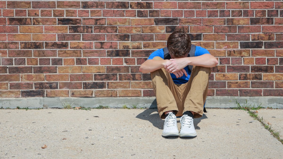 A depressed, upset student sits outside a school. (Shutterstock Photo)