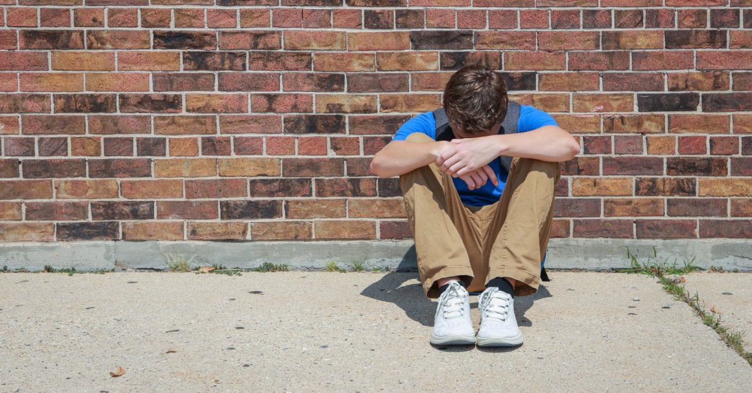 A depressed, upset student sits outside a school. (Shutterstock Photo)
