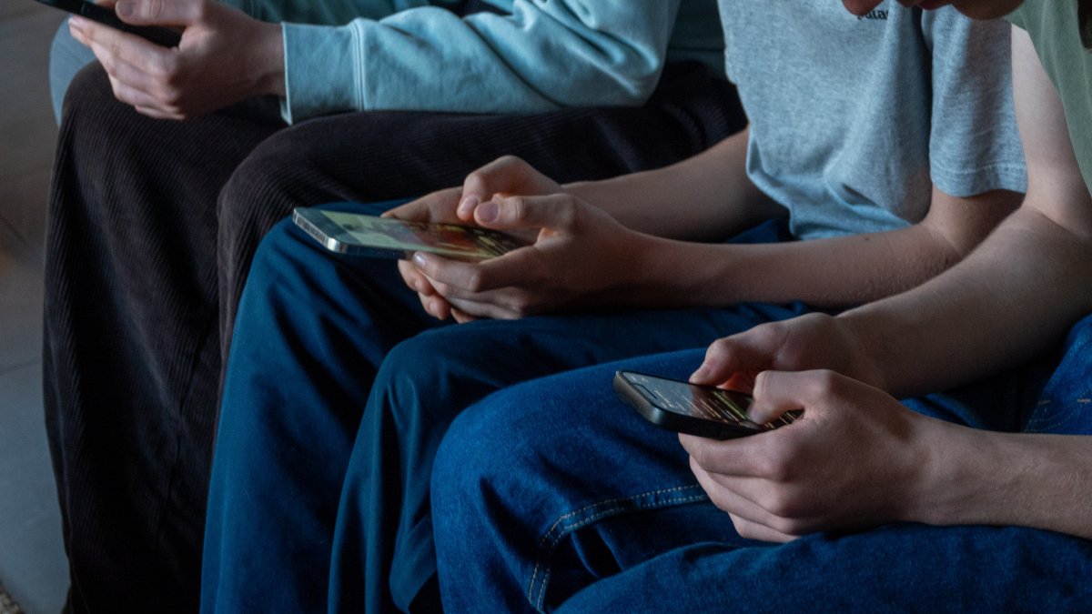 Three teenage boys look at their smartphone screens, Morzine, France, April 11, 2026. (Getty Images Photo)