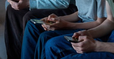 Three teenage boys look at their smartphone screens, Morzine, France, April 11, 2026. (Getty Images Photo)