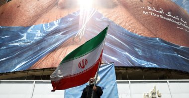 A man holds an Iranian flag near an anti-U.S. billboard depicting U.S. President Donald Trump and the Strait of Hormuz, in Tehran, Iran, May 2, 2026. (Reuters Photo)