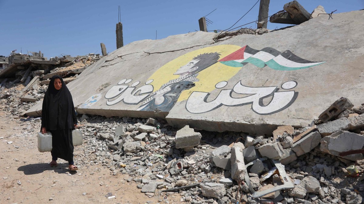 A displaced Palestinian woman carries water containers as she walks past graffiti painted on the rubble of a building destroyed in an Israeli attack at the Jabalia refugee camp, northern Gaza Strip, Palestine, April 13, 2026. (AFP Photo)
