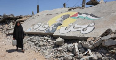 A displaced Palestinian woman carries water containers as she walks past graffiti painted on the rubble of a building destroyed in an Israeli attack at the Jabalia refugee camp, northern Gaza Strip, Palestine, April 13, 2026. (AFP Photo)