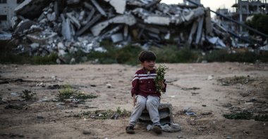 A Palestinian boy sitting on a breeze block in front of destroyed buildings, holds a bunch of spring flowers in the Bureij Palestinian refugee camp in the central Gaza Strip, May 2, 2026. (AFP Photo)