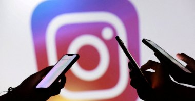 Teenagers pose for a photo while holding smartphones in front of a Facebook logo in this illustration, Sept. 11, 2025. (Reuters Photo)