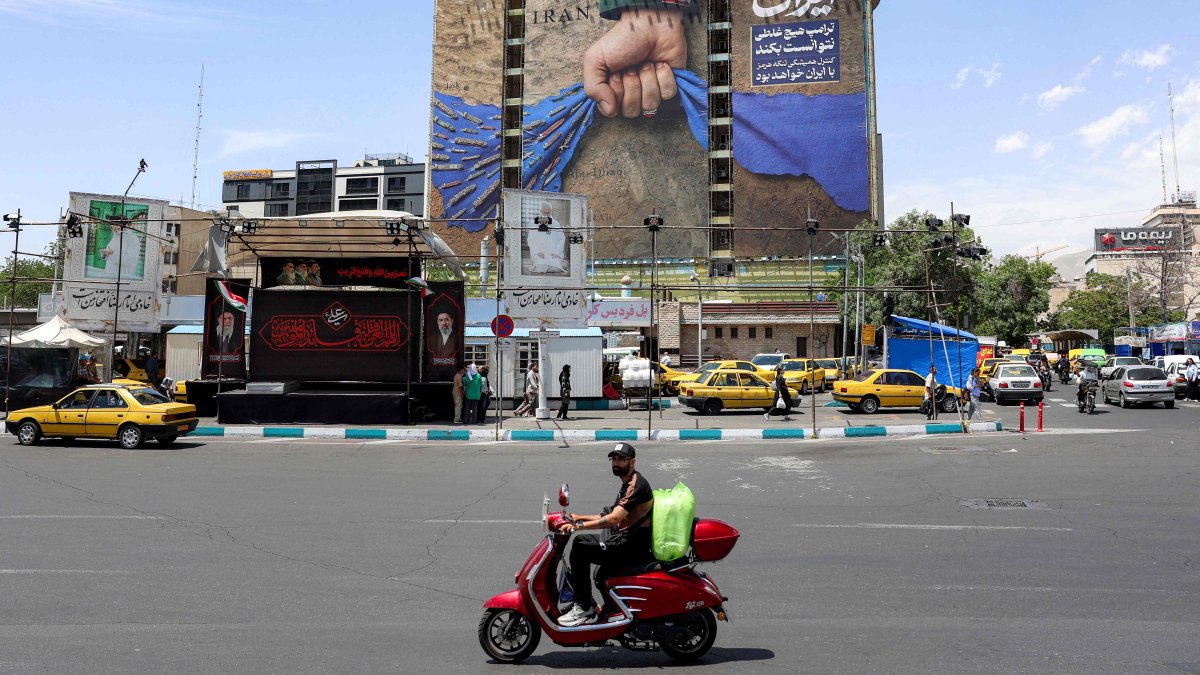 A motorist rides a scooter along a street near a billboard on the facade of a building depicting the Strait of Hormuz with a caption in Persian reading "Forever in Iran’s Hand," at Vanak Square in Tehran, May 6, 2026. (AFP Photo)
