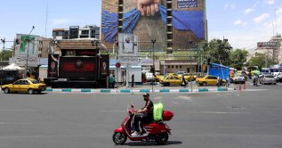 A motorist rides a scooter along a street near a billboard on the facade of a building depicting the Strait of Hormuz with a caption in Persian reading "Forever in Iran’s Hand," at Vanak Square in Tehran, May 6, 2026. (AFP Photo)