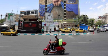 A motorist rides a scooter along a street near a billboard on the facade of a building depicting the Strait of Hormuz with a caption in Persian reading "Forever in Iran’s Hand," at Vanak Square in Tehran, May 6, 2026. (AFP Photo)