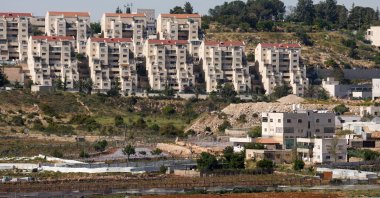The illegal Kiryat Arba settlement appears in the background near Palestinian houses adjacent to road 60, near Hebron, in the Israeli-occupied West Bank, May 7, 2026. (Reuters Photo)