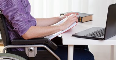 A man in a wheelchair works at his desk. (Shutterstock Photo) 