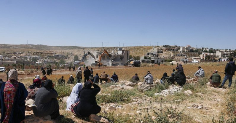 Palestinians watch as Israeli security forces stand guard while excavators demolish a Palestinian house in the village of al-Dirat near Yatta town in Hebron, occupied West Bank, May 4, 2026. (AFP Photo)