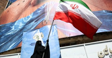 A woman holds Iran’s national flag in front of a huge anti-U.S. billboard referring to U.S. President Donald Trump and the Strait of Hormuz at Valiasr Square in Tehran, Iran, May 11, 2026. (EPA Photo)