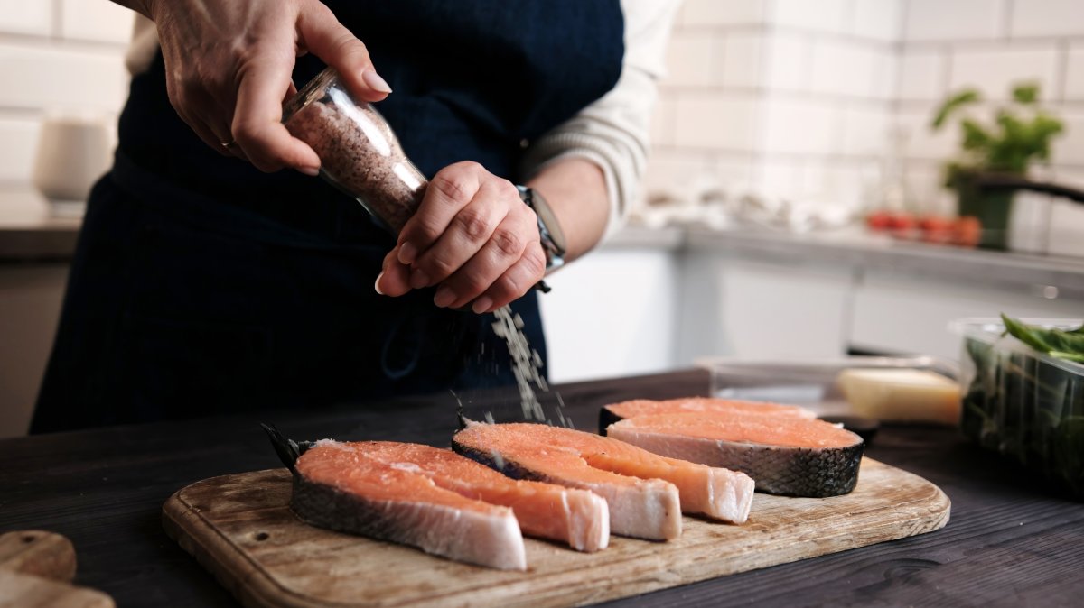 A woman adds salt to raw red salmon while preparing a meal. (Shutterstcok Photo) 