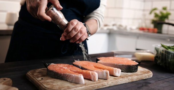 A woman adds salt to raw red salmon while preparing a meal. (Shutterstcok Photo) 