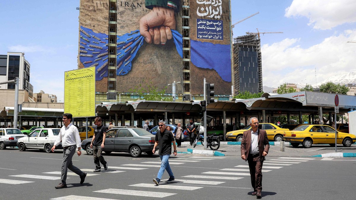 People cross a street near a billboard on the facade of a building depicting the Strait of Hormuz with a caption in Persian reading "Forever in Iran’s Hand," Tehran, Iran, May 6, 2026. (AFP Photo)