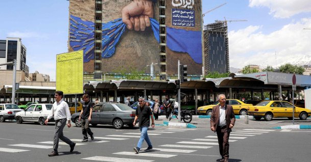 People cross a street near a billboard on the facade of a building depicting the Strait of Hormuz with a caption in Persian reading "Forever in Iran’s Hand," Tehran, Iran, May 6, 2026. (AFP Photo)
