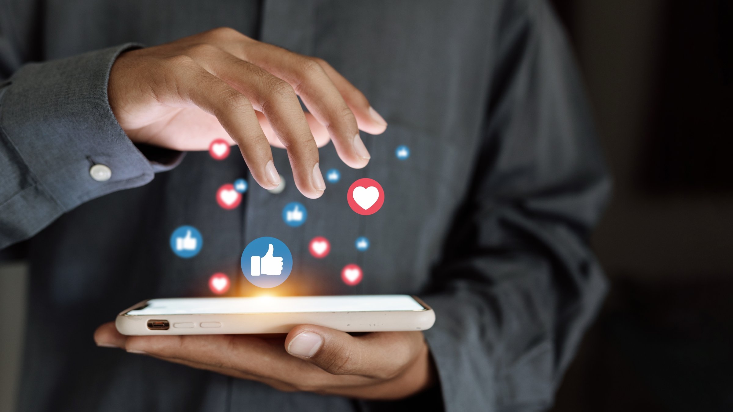 A close-up of a hand using a smartphone with social media icons floating above the screen. (Shutterstock Photo)